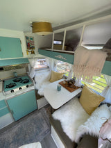 Cozy RV rental interior with vintage teal kitchen, dining nook with fluffy seats, & a bunk bed.