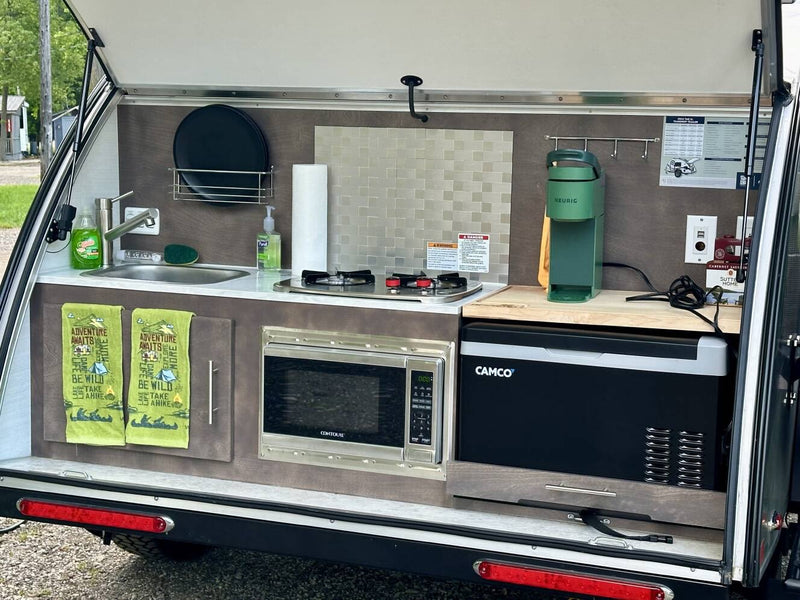  and an outdoor mat in a wooded campsite.|This rv rental features a compact outdoor kitchen with a sink — photo 5