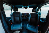 The front interior of a Storyteller Overland van with black leather seats and dashboard, great for an RV rental.