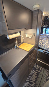 Inside a modern RV rental: a neat kitchenette with sink, faucet, and ample storage, adjacent to a comfy sleeping space.