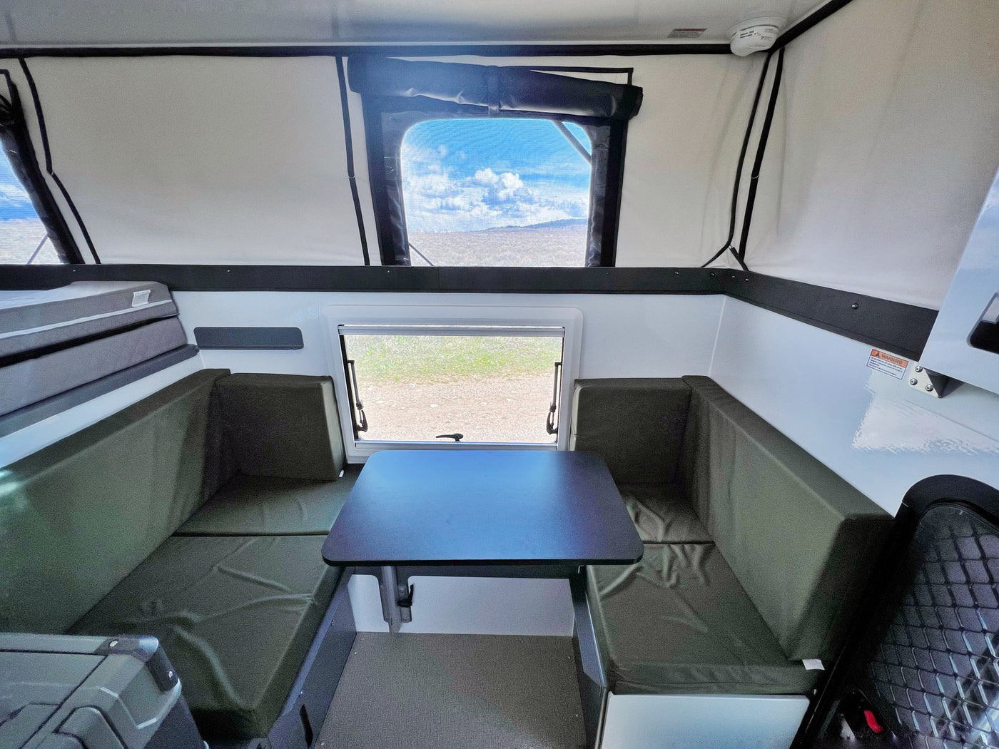 This RV rental offers a spacious pop-up camper interior with a cozy dinette, sleeping area, and panoramic views. — photo 10