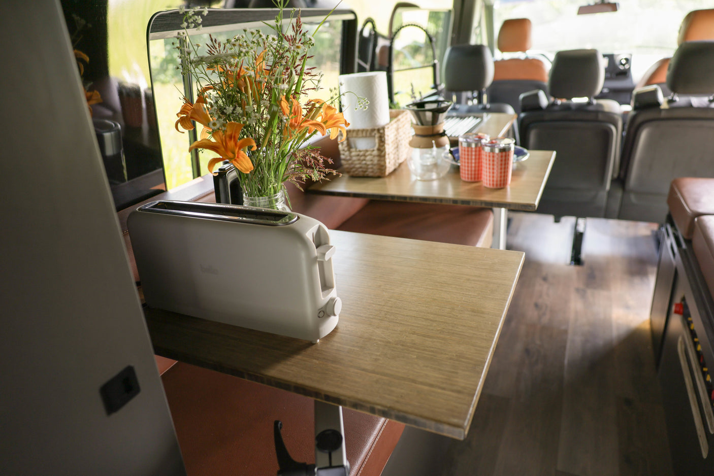 Cozy RV rental interior with a toaster, fresh flowers, and coffee setup on wooden tables, perfect for a road trip.