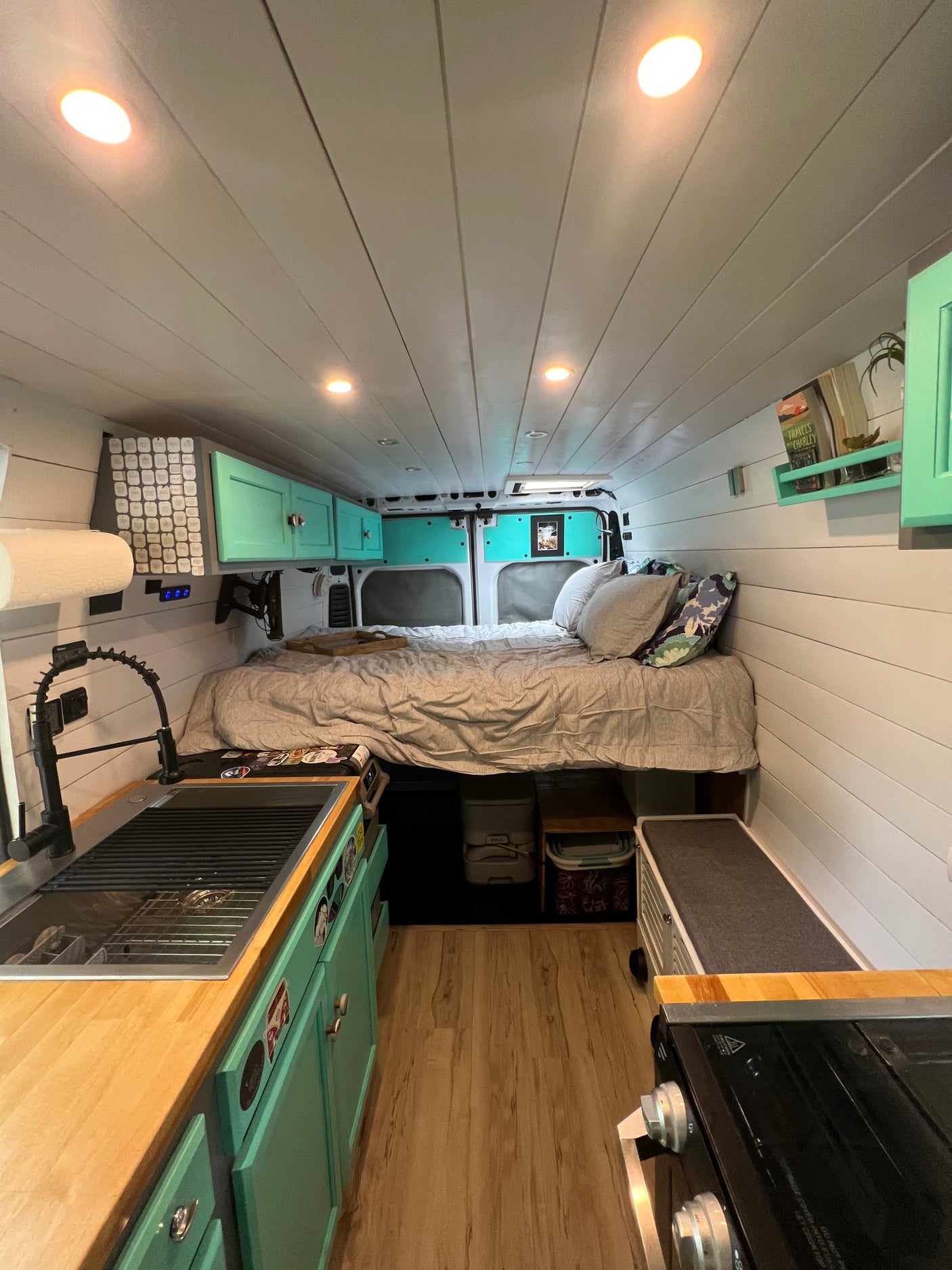Bright RV rental interior: features a comfy bed, compact kitchen with sink, and teal cabinets. Perfect for trips!
