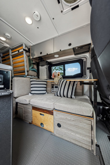 Cozy RV rental interior with bench seating, pillows, window view, and ample storage, perfect for mobile living.