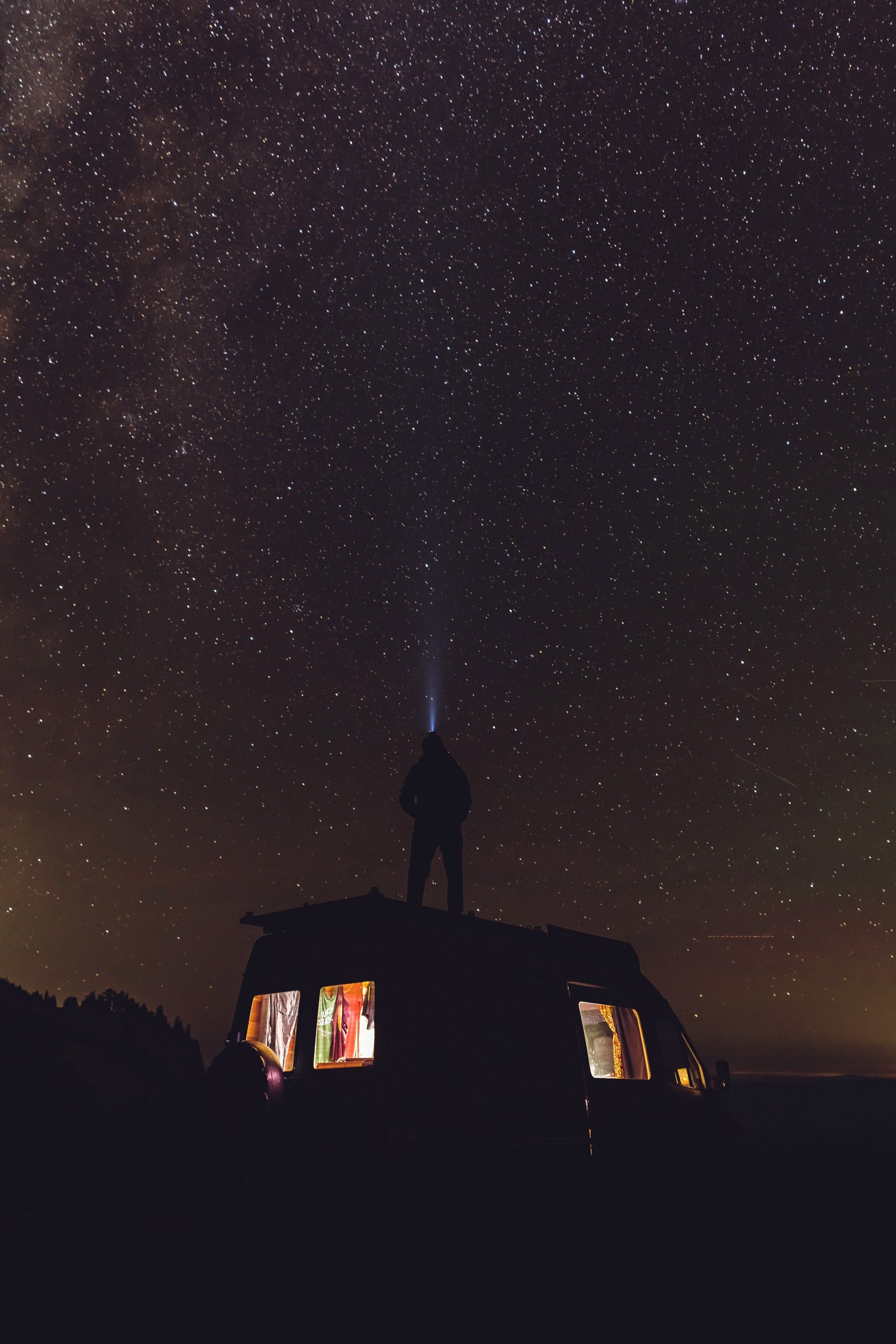 Experience epic stargazing with an **RV rental**. A person on a camper van roof beams a light into a dazzling, star-filled night sky.
