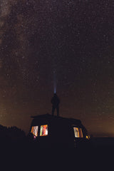 Experience epic stargazing with an **RV rental**. A person on a camper van roof beams a light into a dazzling, star-filled night sky.