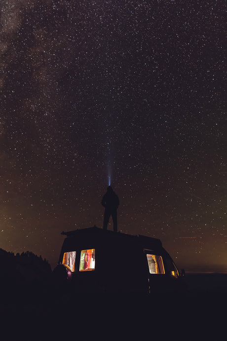 Experience epic stargazing with an **RV rental**. A person on a camper van roof beams a light into a dazzling, star-filled night sky.