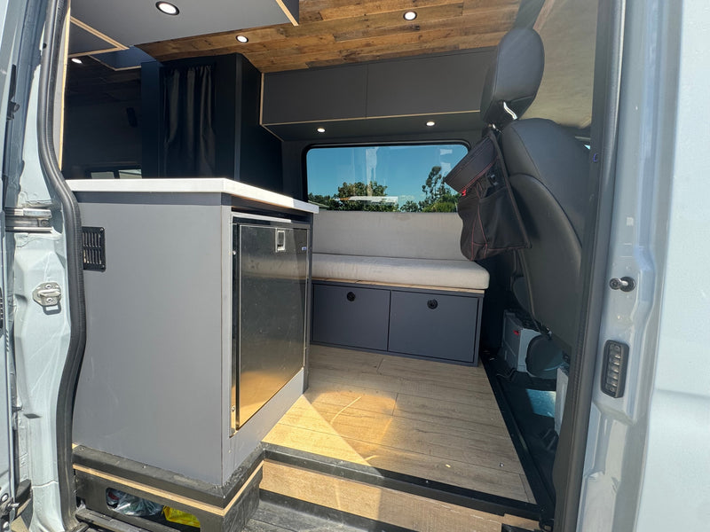 Modern camper van interior, seen from the open side door. Features a kitchen with fridge, bench seat storage. Ideal for an rv rental. — photo 4