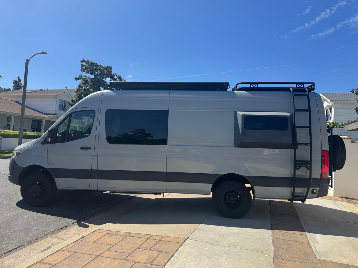 Side view of a light grey custom camper van with off-road tires, roof rack, and ladder. Perfect for an rv rental trip. — photo 3