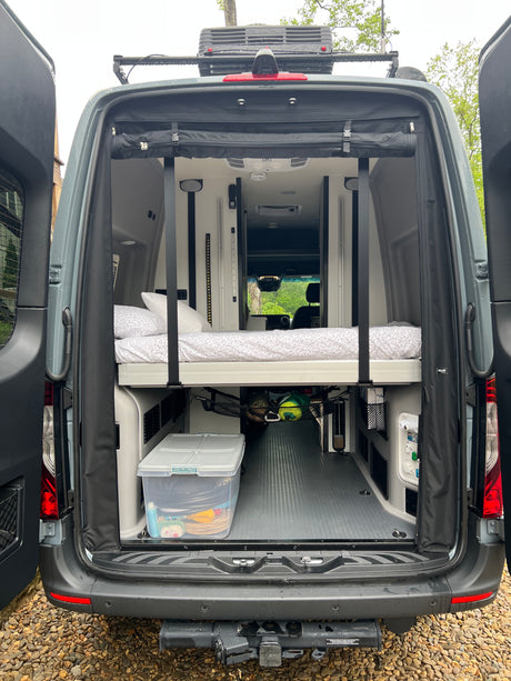 Explore a modern RV rental: open back doors reveal a comfortable elevated bed and versatile storage.