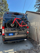 A dark gray Thor RV rental with a Camping World license plate, carrying a red Orbea road bike on its rear rack.