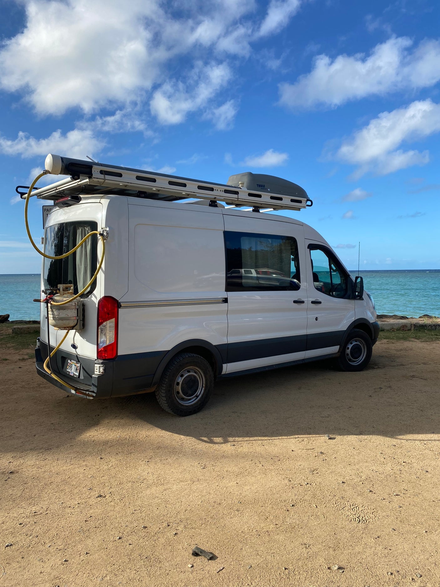 Experience a scenic RV rental! White camper van by the bright blue ocean, ready for adventure on the Kauai coast.