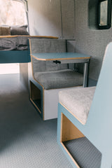 Clean RV rental interior: compact seating, removable table, and comfortable bed. Modern campervan design for travel.