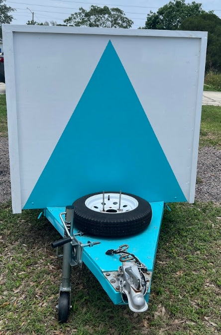 Custom blue trailer for RV rental advertising, featuring a striking white and blue triangle sign, with a spare tire.